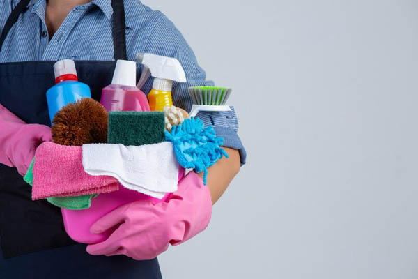 Woman holds cleaning products gloves rags basin white wall 